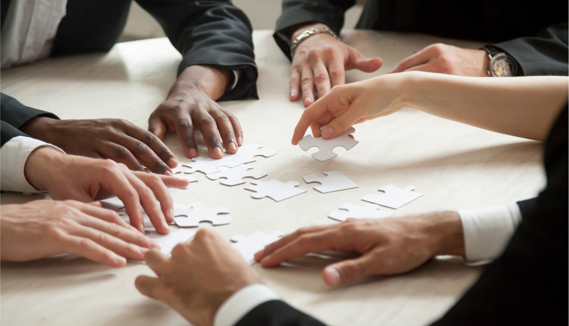 In this close-up photo, a diverse group of individuals is gathered around a table, each holding uniquely shaped puzzle note cards. Their hands are actively engaged, arranging and discussing the puzzle-shaped cards that symbolize brainstorming for a business idea. The hands belong to a mix of genders and ethnicities, highlighting diversity in the group. The note cards come in various colors, and participants are seen arranging and connecting them, suggesting collaboration and problem-solving. The close-up view captures the intricate details of their hands and the puzzle pieces, emphasizing the cooperative and creative nature of the brainstorming session.